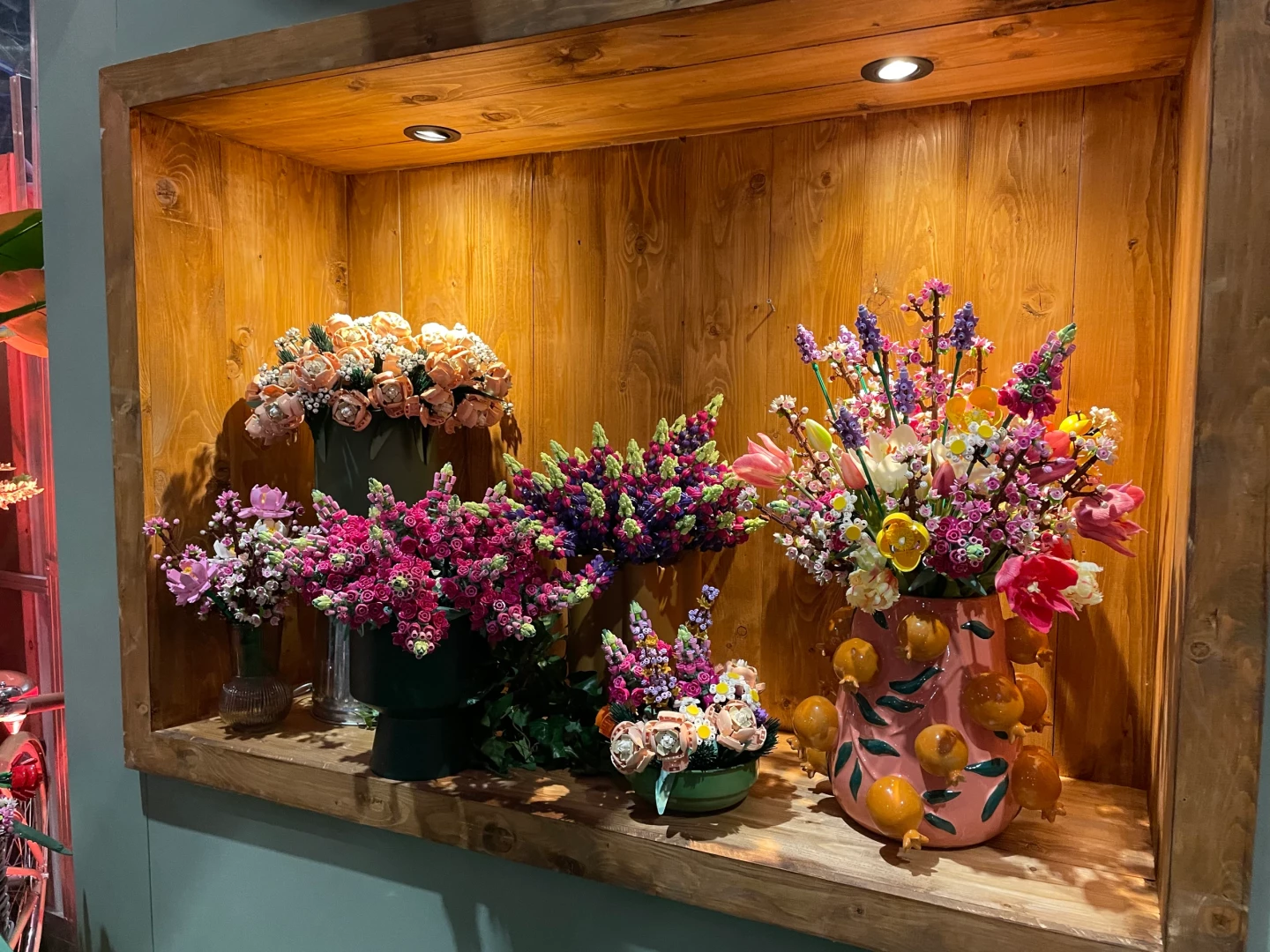 Een houten schap gevuld met LEGO bloemstukken, waaronder blauwe en roze bloemen.